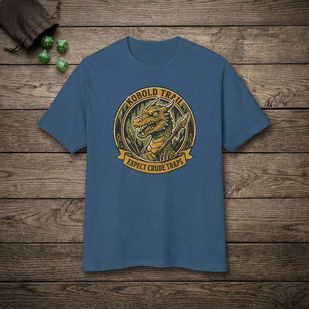 Deadpan national park style graphic tee warning tabletop adventurers to watch their step for crude traps along the kobold trail, shown laid flat among dice