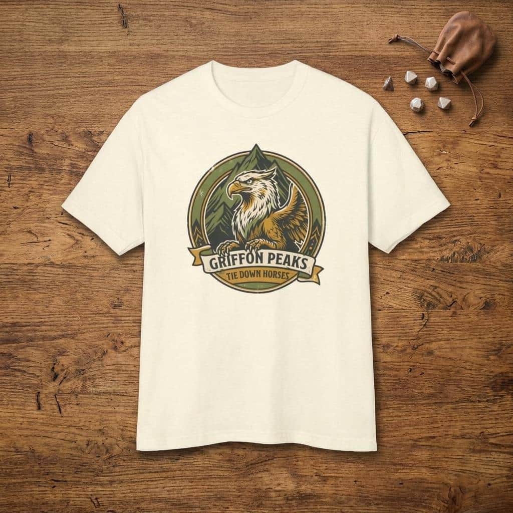 Photo 6 of 15: Vintage national park parody tee featuring a noble mountain griffon alongside a deadpan ranger warning for traveling adventurers to keep their prized mounts secured, shown laid flat among dice