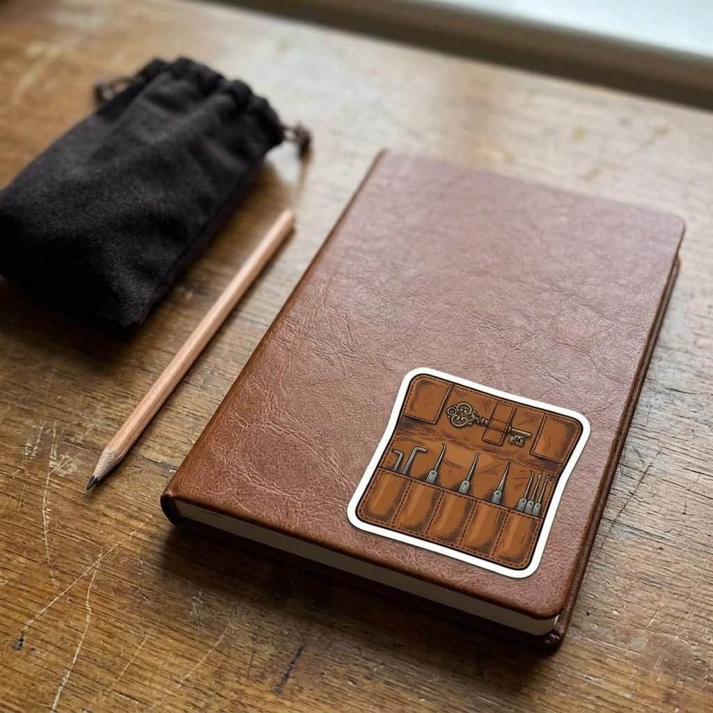 Photo 7 of 11: A detailed kiss-cut vinyl decal featuring an unrolled rogue's leather lockpick kit, shown on a notebook