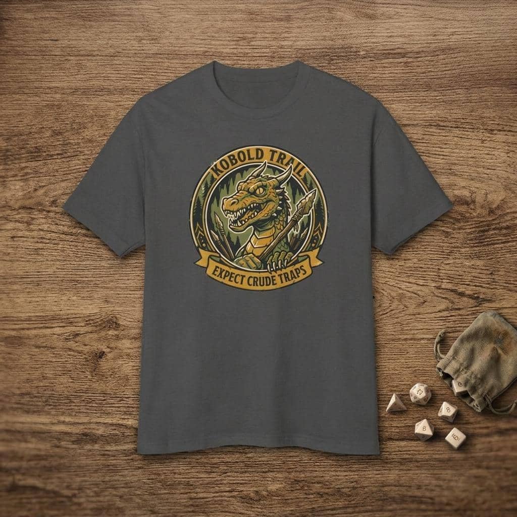 Deadpan national park style graphic tee warning tabletop adventurers to watch their step for crude traps along the kobold trail, shown laid flat among dice
