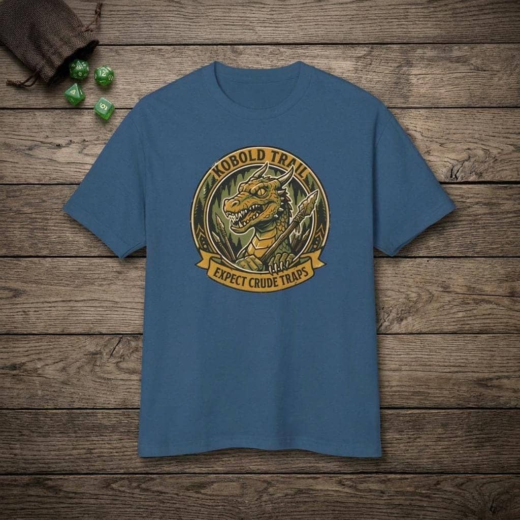 Deadpan national park style graphic tee warning tabletop adventurers to watch their step for crude traps along the kobold trail, shown laid flat among dice